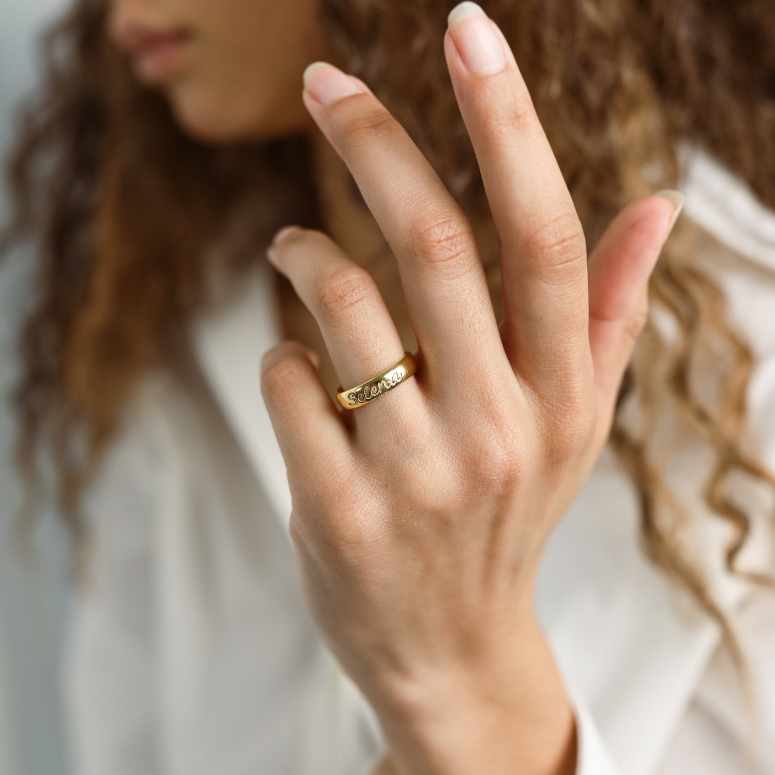 A person with curly hair wears the Ann Half Round Ring, featuring engraved text, elegantly paired with a white shirt.