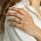 A hand wearing the Birthstone Signet Ring, a gold vintage piece with a blue stone, rests on a white shirt.