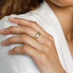 A hand with manicured nails and light brown skin wears the Audrey Ring, an elegant everyday accessory, as it rests on white fabric.