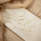 Three Mama Letter Necklaces with "mama" in script are shown on beige fabric and a stone slab—an ideal gift for mothers or to honor motherhood.