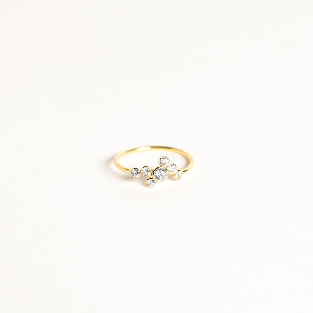 The Cluster Birthstone Ring features seven small round diamonds set in an asymmetric cluster on a white backdrop—ideal for those who appreciate classic design.