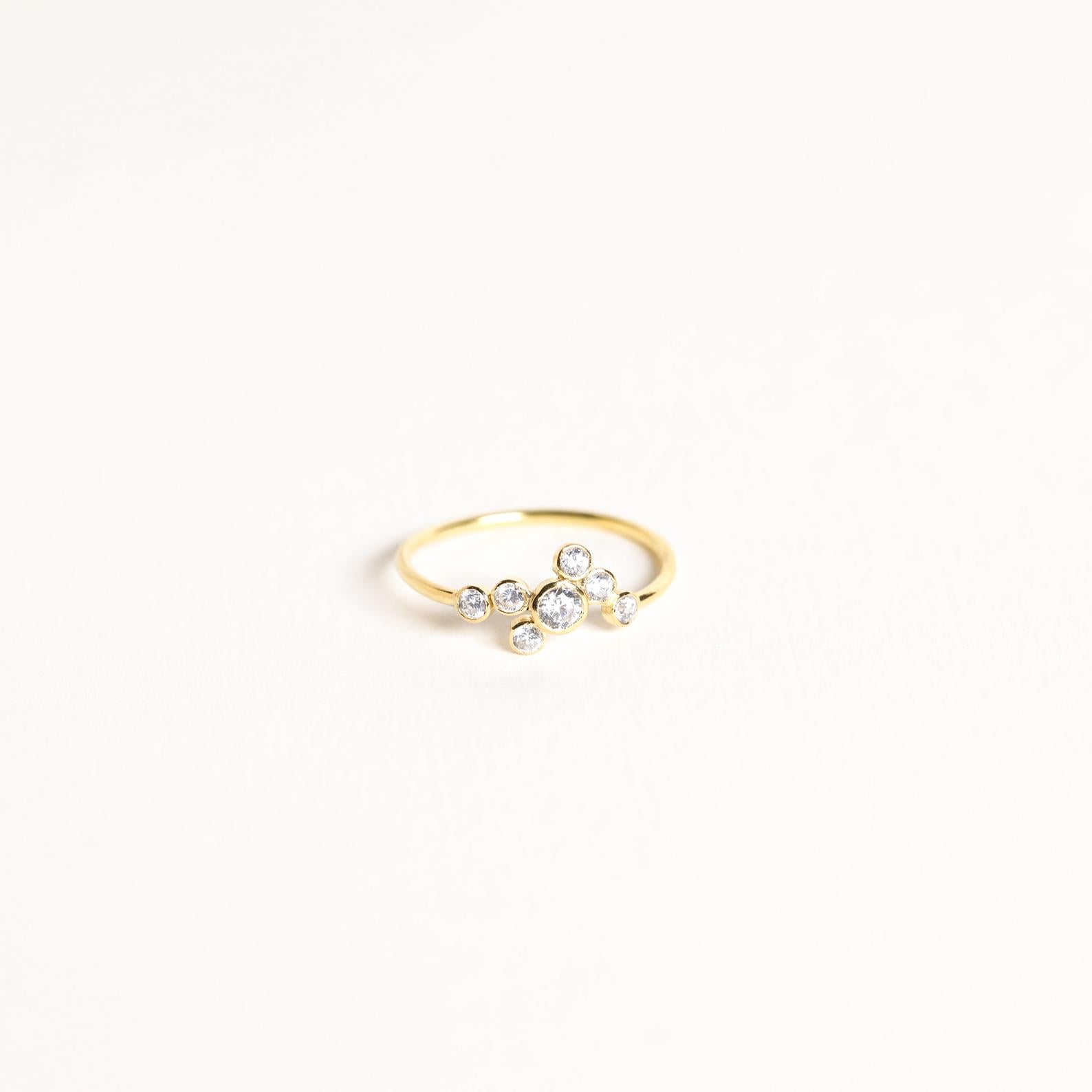 The Cluster Birthstone Ring features seven small round diamonds set in an asymmetric cluster on a white backdrop—ideal for those who appreciate classic design.