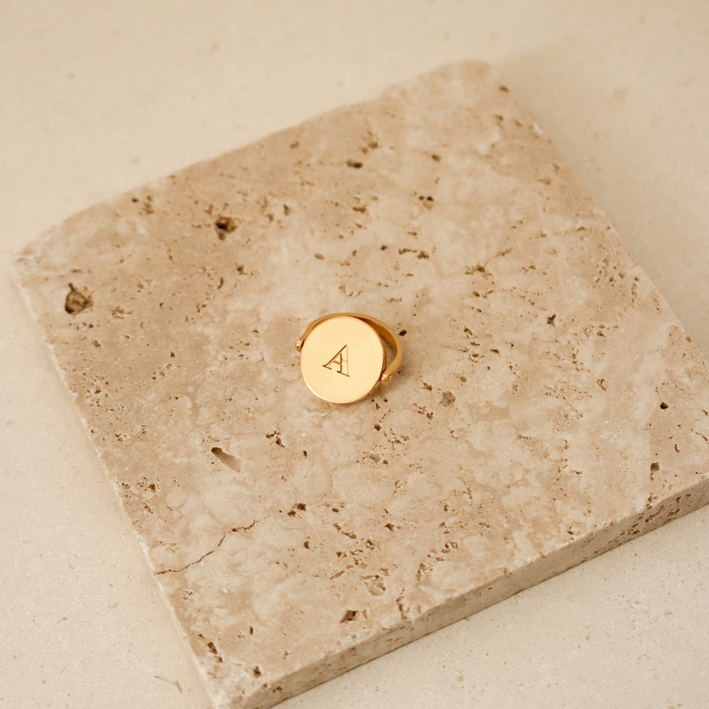 Spinner Pendant Necklace with the letter A engraved, featuring a subtle spinning detail, displayed on a textured beige stone tile.