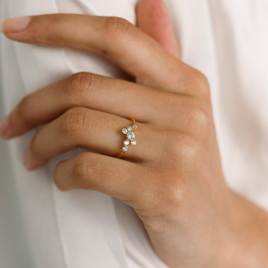 A hand wearing the Cluster Birthstone Ring with sparkling clustered round diamonds rests on a white fabric background.