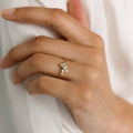 A hand wearing the Cluster Birthstone Ring with sparkling clustered round diamonds rests on a white fabric background.