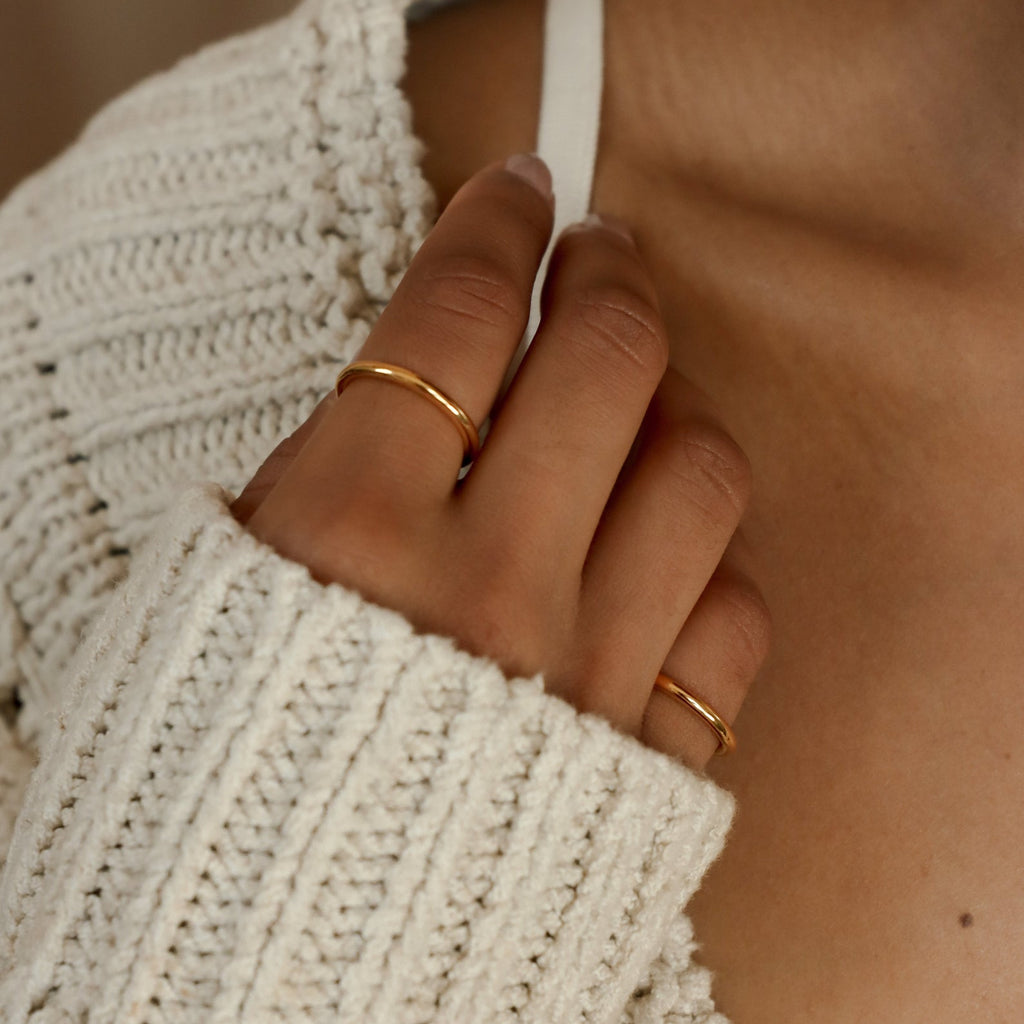 A hand wearing the Minimal Stacking Ring touches a white strap while dressed in a cream knit sweater.