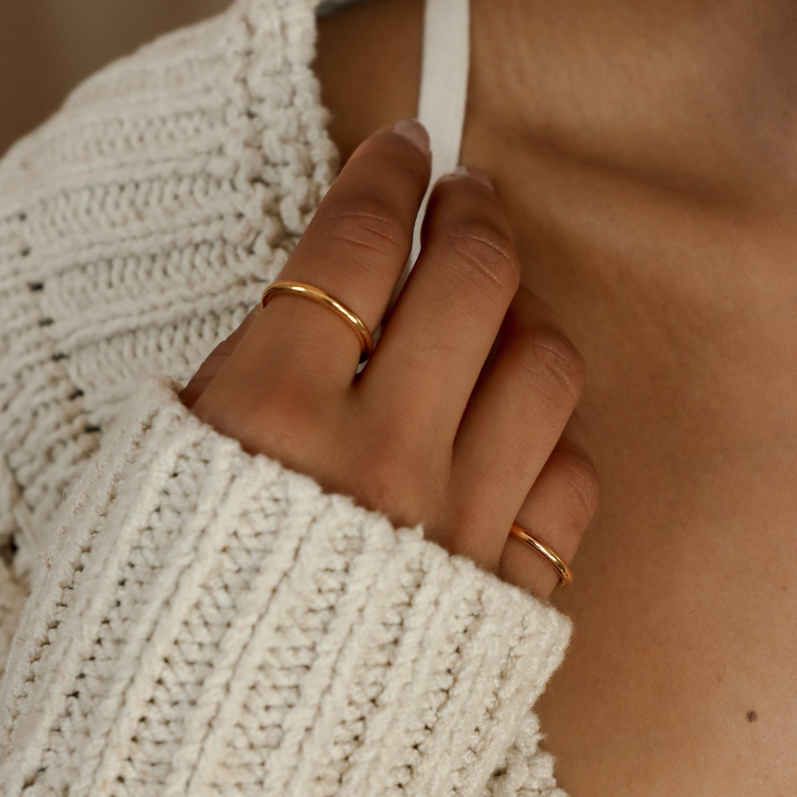A hand wearing the Minimal Stacking Ring touches a white strap while dressed in a cream knit sweater.