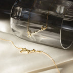 Two Venice Name Necklaces, "Amanda" and "Peyton," in elegant script, displayed on glass and satin. These dainty gold necklaces are perfect personalized jewelry pieces to elevate any look.