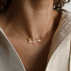 The Summer Name Necklace is a gold personalized necklace displaying the name Amanda in an elegant script font, shown worn by someone in a cream-colored shirt.