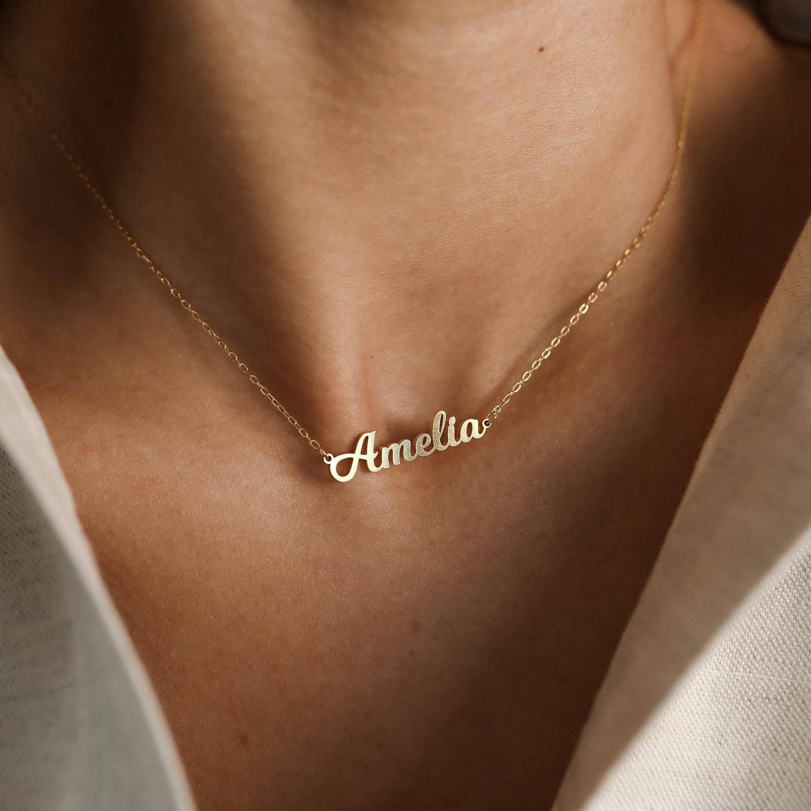 Close-up of a Mellow Name Necklace featuring the name Amelia in gold cursive, worn on a woman's neck.