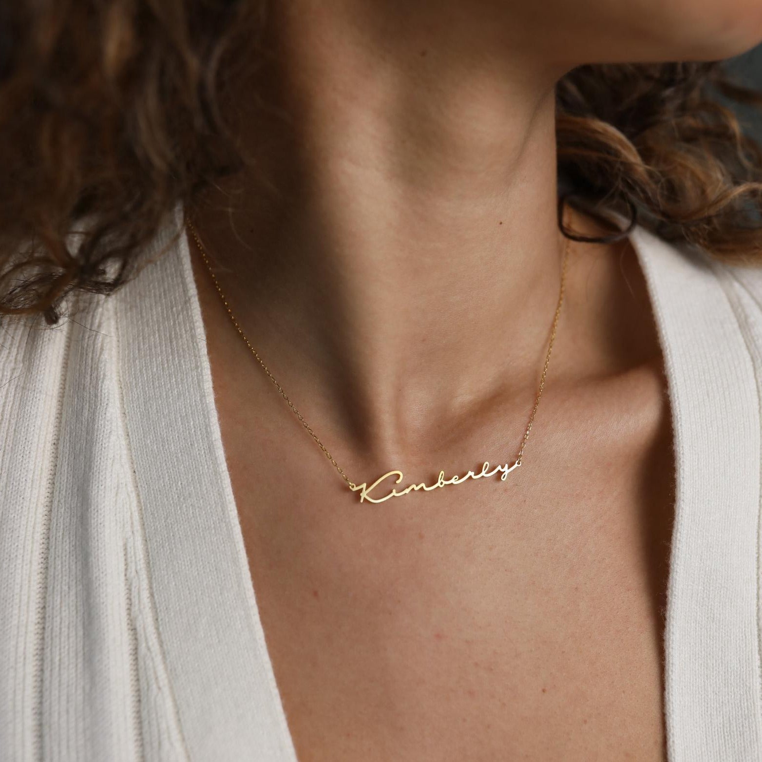 The Minimal Name Necklace in gold, featuring "Kimberly" in script, rests elegantly around her neck—a personalized gift to treasure.