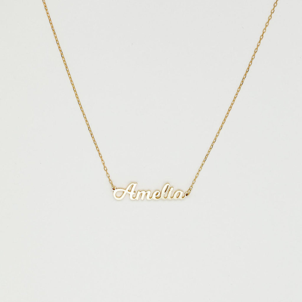 The Mellow Name Necklace features a gold chain and a pendant spelling "Amelia" in elegant cursive, making it an ideal personalized necklace for any special occasion.