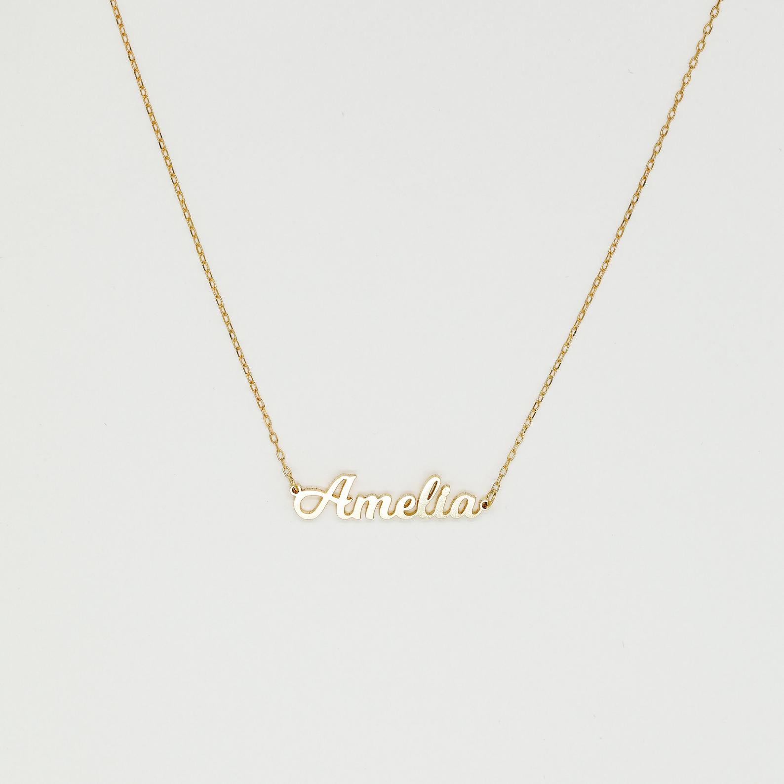 The Mellow Name Necklace features a gold chain and a pendant spelling "Amelia" in elegant cursive, making it an ideal personalized necklace for any special occasion.
