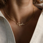 Minimal style Carrie Name Necklace in Figaro Chain, gold finish with "Sophia" nameplate, worn elegantly over a white shirt with an open collar.