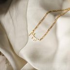 The Summer Name Necklace in Figaro Chain features a cursive font nameplate pendant on soft, cream-colored fabric—making it the ideal accessory for summer.