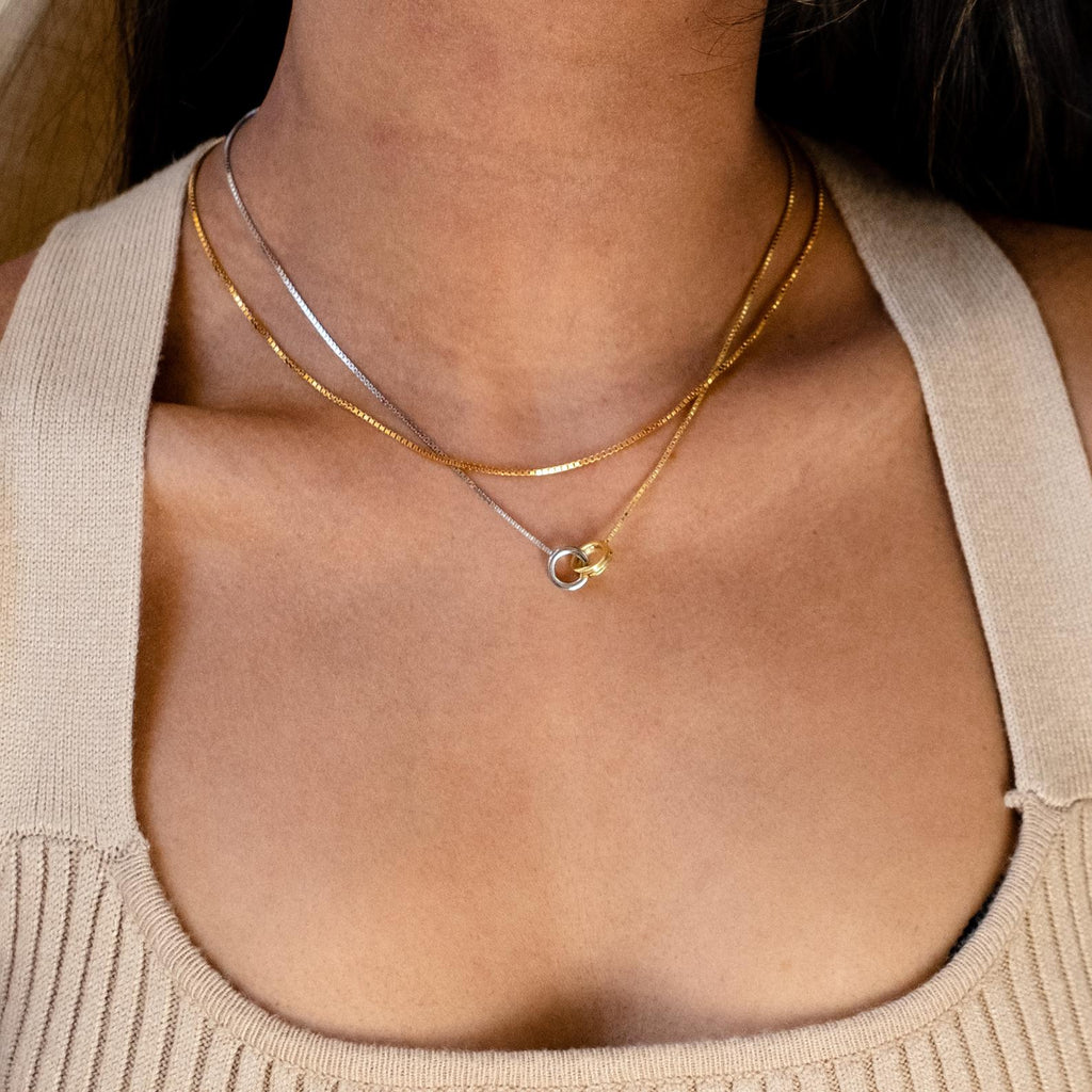 A woman wears a beige top with the Interlocking Circles Necklace, featuring layered silver and gold chains with interlocking circle accents around her neck.