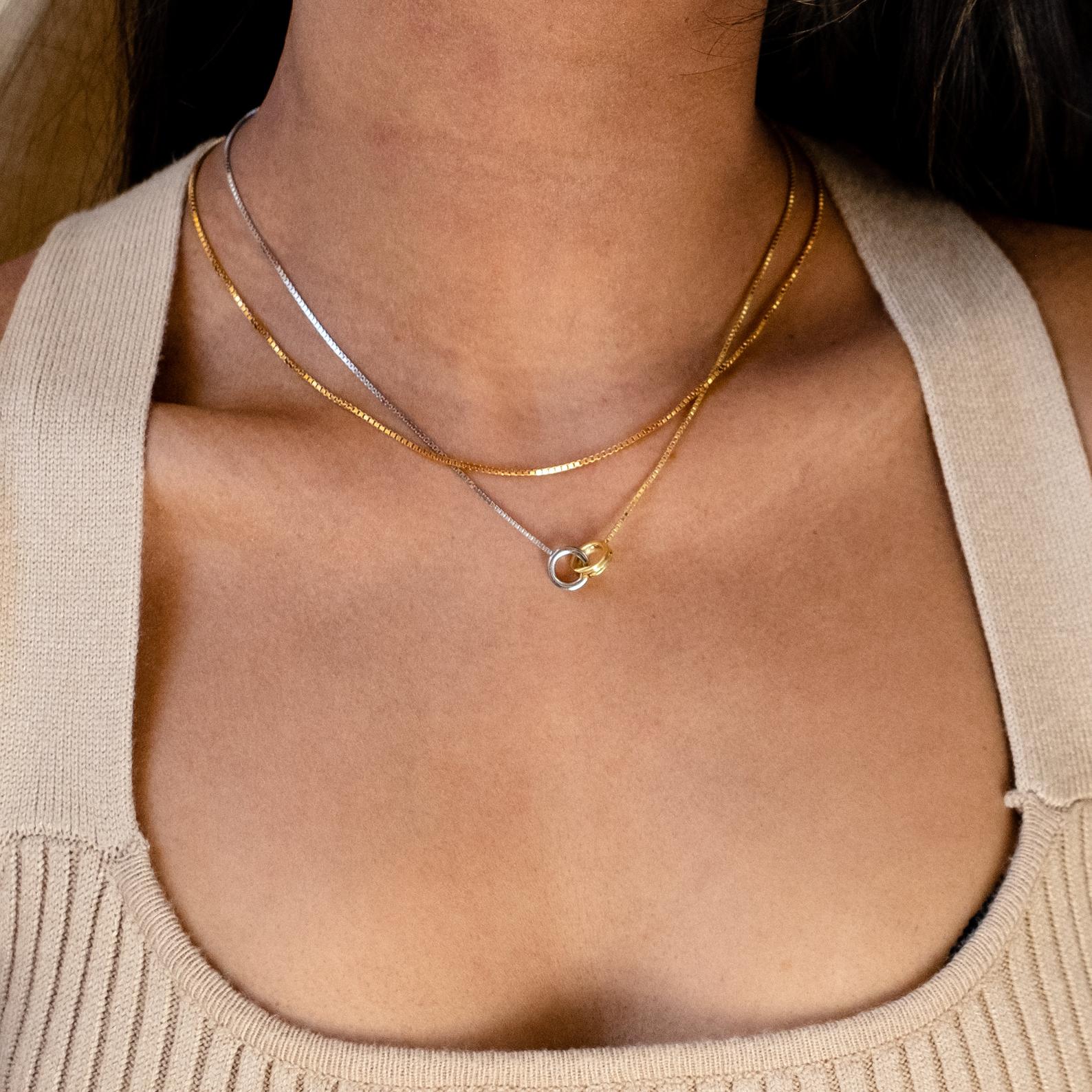 A woman wears a beige top with the Interlocking Circles Necklace, featuring layered silver and gold chains with interlocking circle accents around her neck.