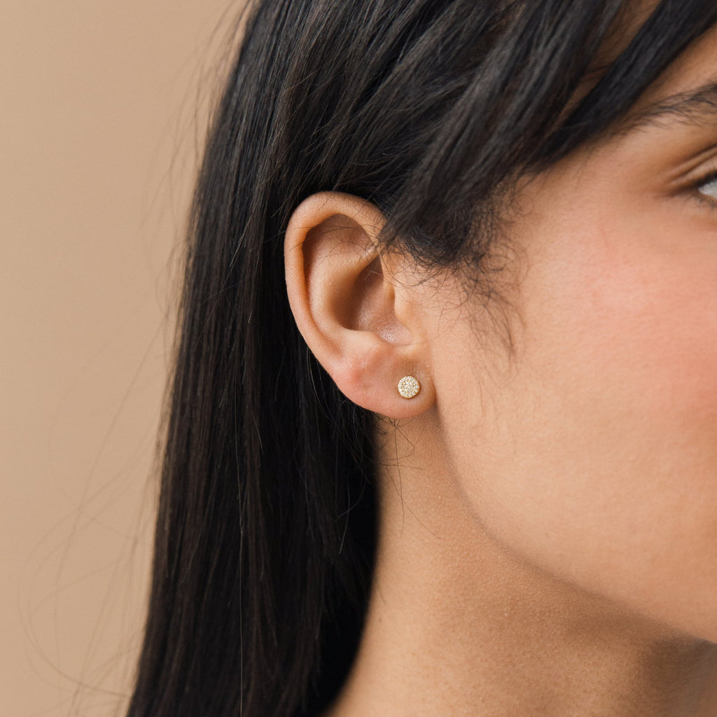Close-up of a woman's ear with straight dark hair, wearing Pave Round Studs—small, round gold earrings ideal for those who prefer subtle glam jewelry over larger or sparkling pave styles.