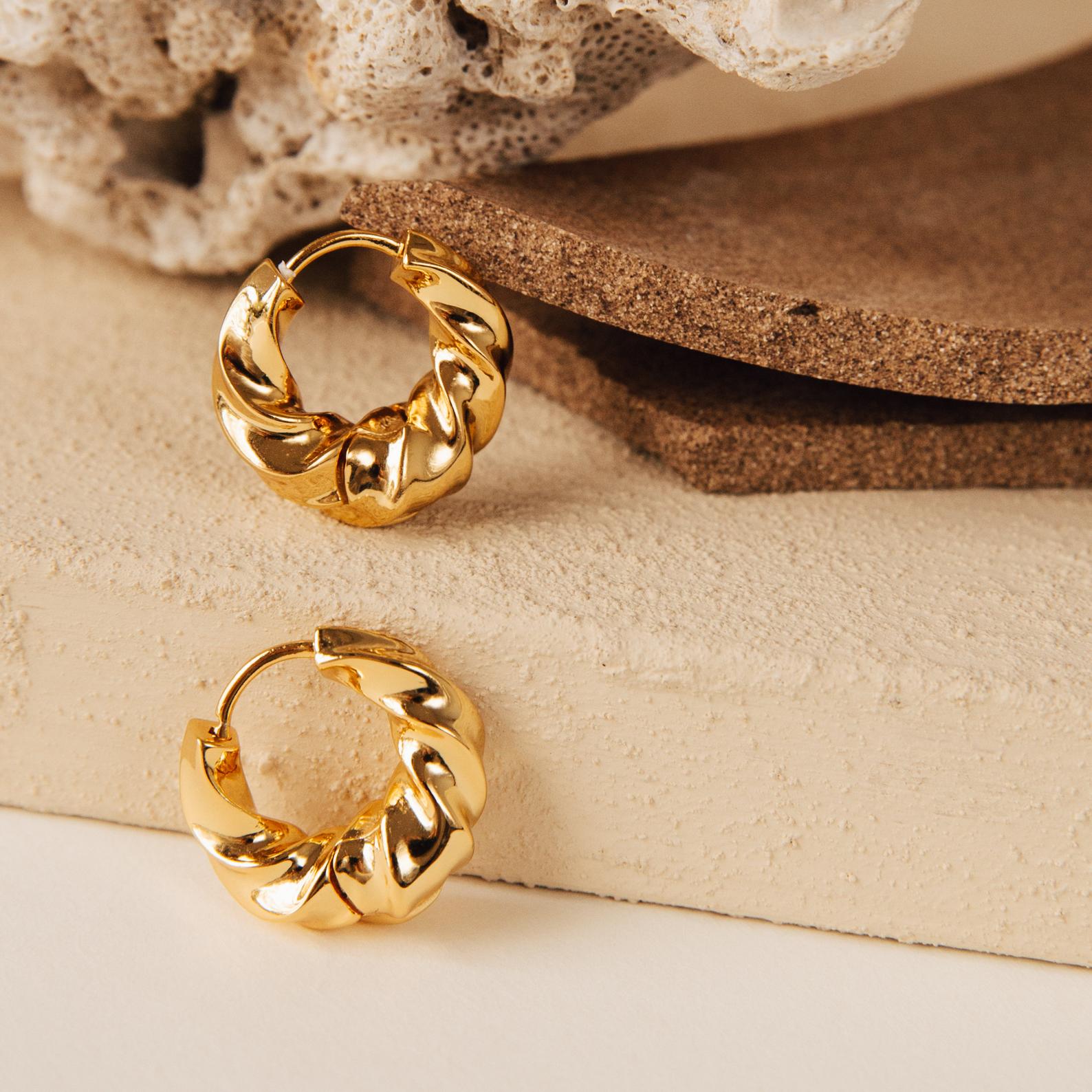 Two Diana Hoops, inspired by modern design, are shown on neutral textured surfaces with coral in the background.