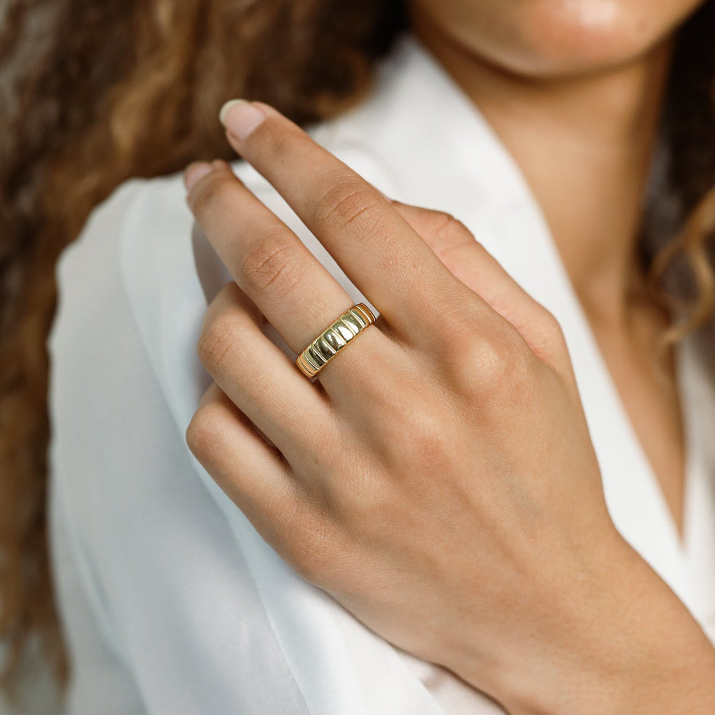 A woman wears the Audrey Ring, featuring a ridged gold design, with a white blouse—an everyday essential for understated elegance.