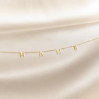 The Mama Letter Necklace, with charms spelling MAMA, is displayed on soft cream-colored fabric—a perfect gift to celebrate motherhood.