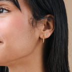 Close-up of a woman's ear with minimal jewelry: a small gold hoop and Pave Bar Studs, adding elegance to her gold earrings collection.