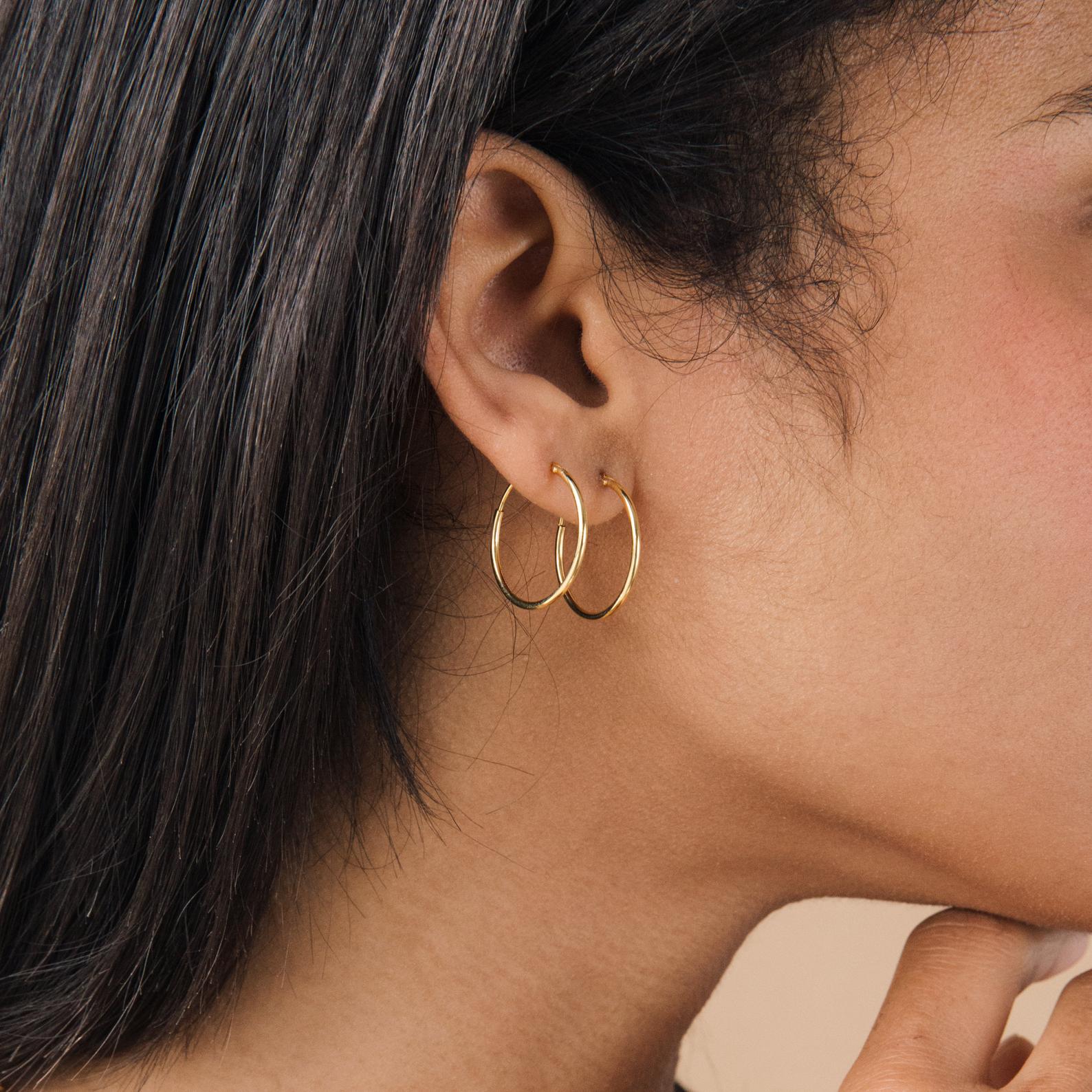 Close-up of a woman wearing Thin Hoop Earrings—two delicate hoops in her ear, hand touching chin—a stylish choice for everyday jewelry.