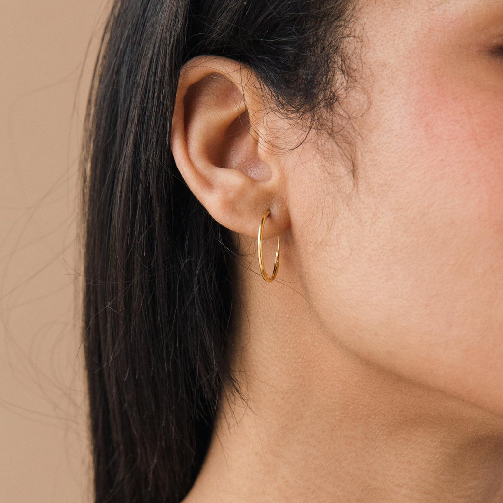 Close-up of a woman's ear with straight dark hair, wearing Thin Hoop Earrings—an elegant and versatile choice for everyday style.
