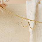 Two Thin Hoop Earrings are displayed on a slender beige stem with a soft white fabric backdrop, showcasing their minimalist design—making these earrings an ideal choice for everyday wear.