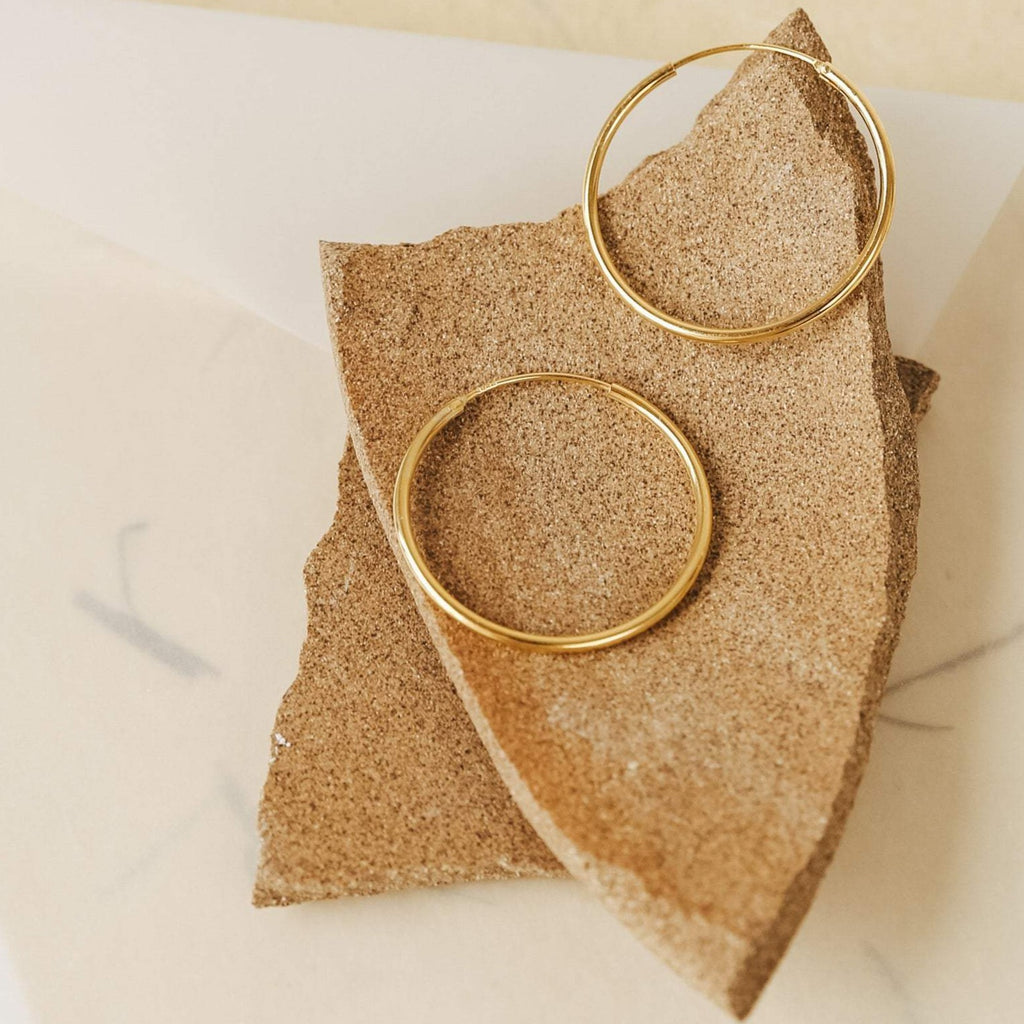 Large Thin Hoops rest on a rough, broken piece of tan stone—a simple yet stylish hoop earring design that easily elevates your everyday look.