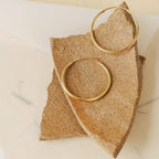 Large Thin Hoops rest on a rough, broken piece of tan stone—a simple yet stylish hoop earring design that easily elevates your everyday look.
