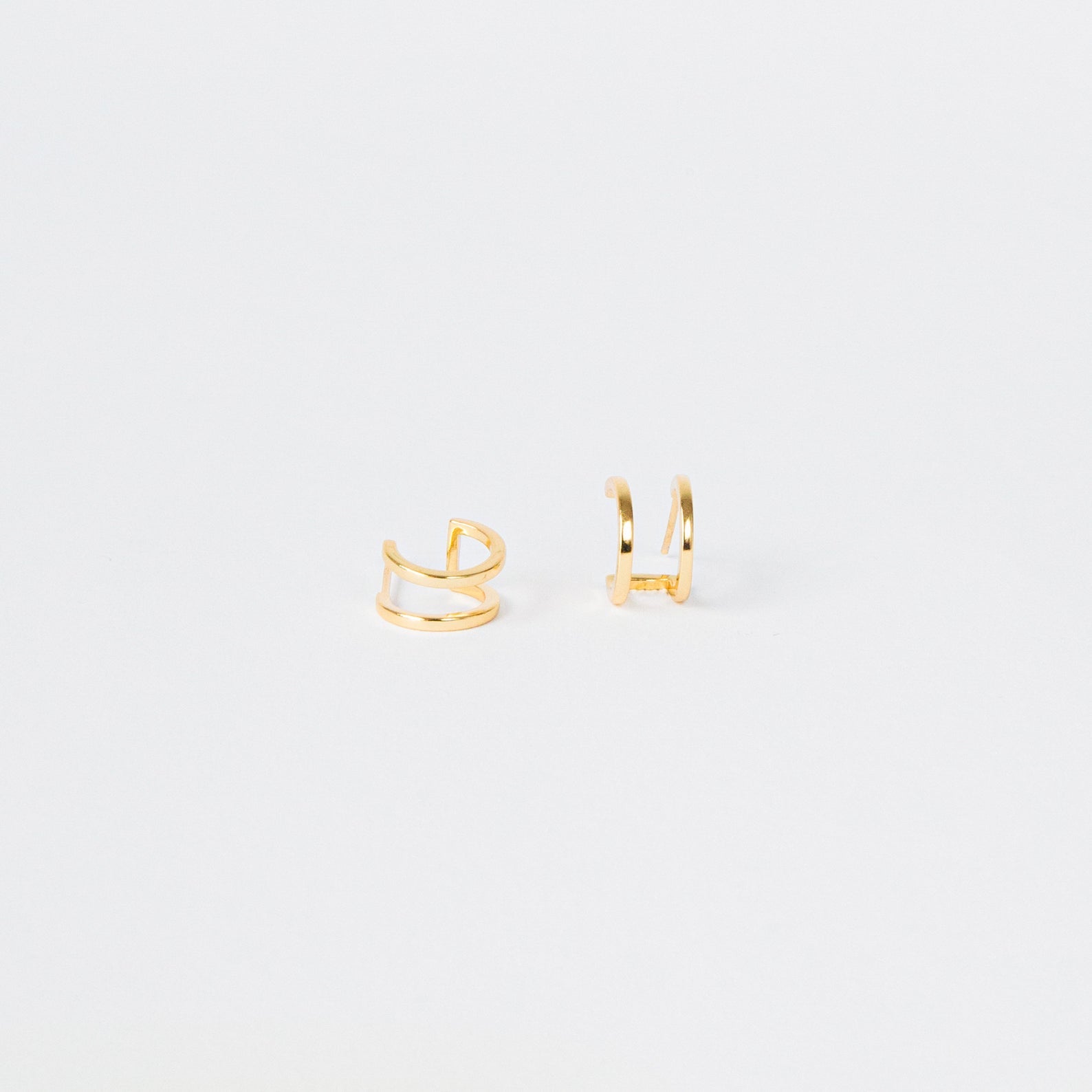 Twin Hoops: Minimalist gold ear cuffs displayed on a plain white background, creating a chic double earring illusion.