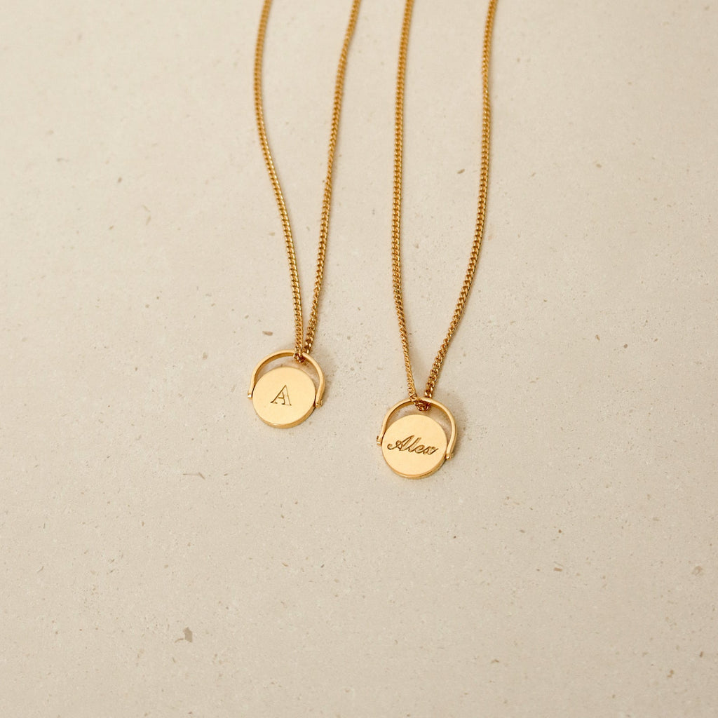 Two gold Spinner Pendant Necklaces with round pendants—one engraved with the letter A, the other with the name Alison—each featuring a unique spinning detail.