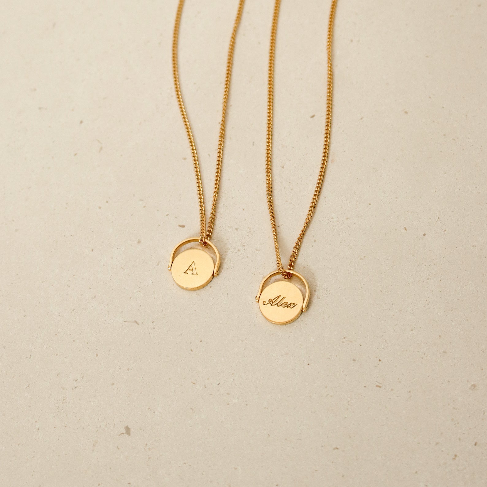 Two gold Spinner Pendant Necklaces with round pendants—one engraved with the letter A, the other with the name Alison—each featuring a unique spinning detail.