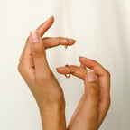 Manicured hands hold the Minimal Stacking Ring and other dainty gold rings against a simple, light background.