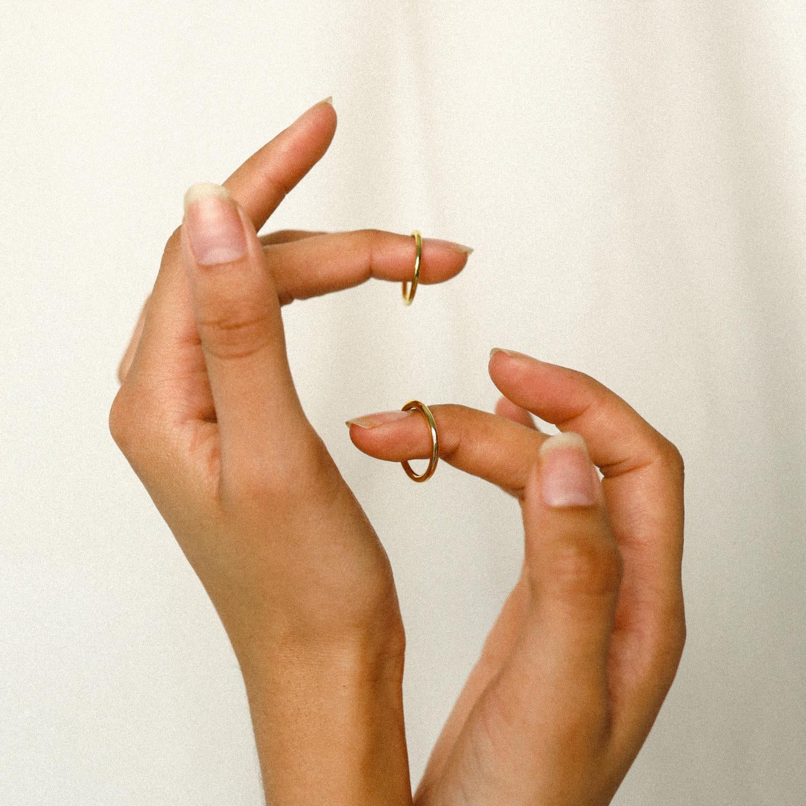 Manicured hands hold the Minimal Stacking Ring and other dainty gold rings against a simple, light background.