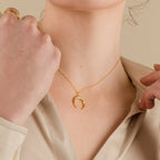 A woman wearing the Crescent Moon Necklace and a gold ring, dressed in a cream-colored blouse.