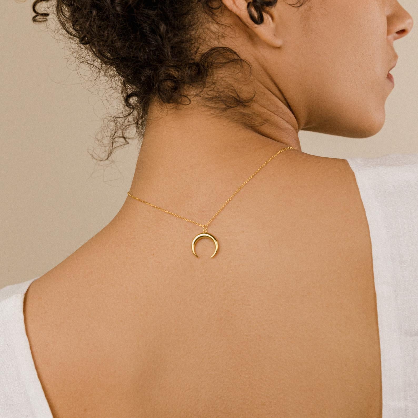 A woman in a white top wears the Crescent Moon Necklace backward on her neck.