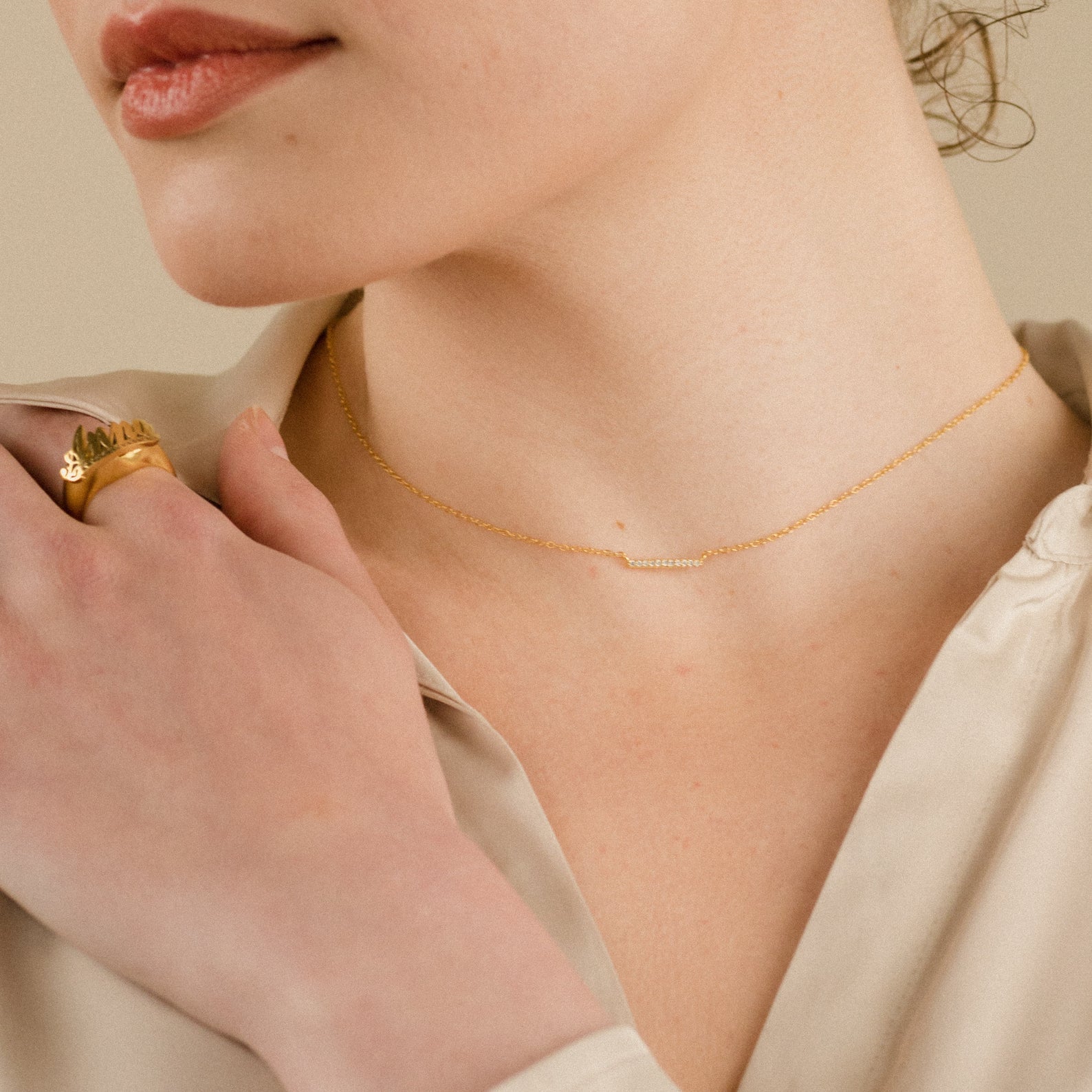 A woman in a cream blouse wears a delicate necklace stack featuring the Pave Bar Necklace and a ring.