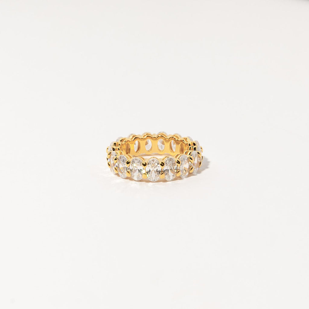 The Alannah Ring features round clear gemstones set all around a gold infinity band—an elegant jewelry piece, showcased on a white background.