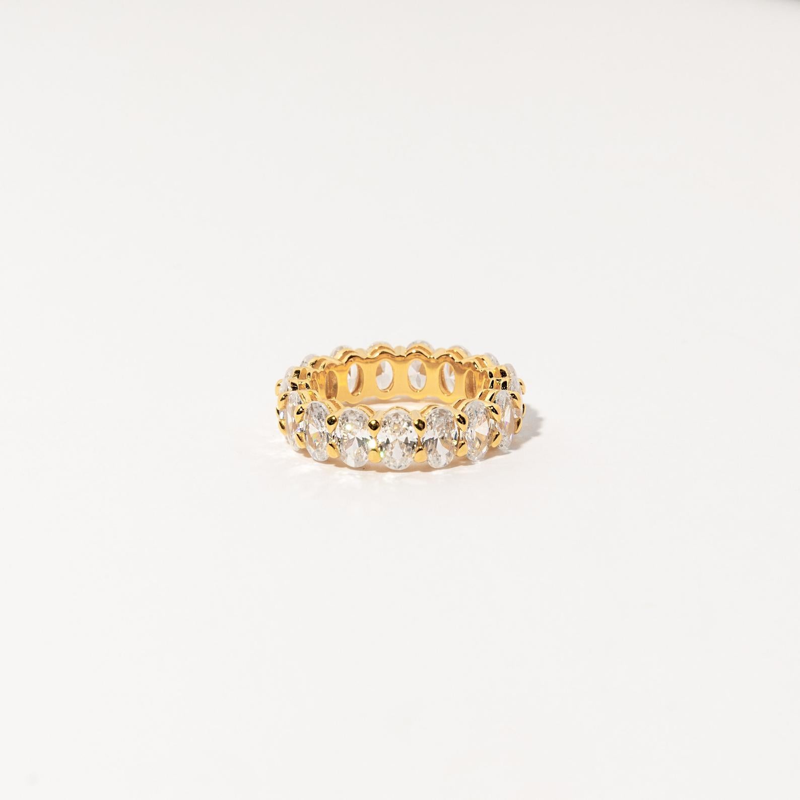 The Alannah Ring features round clear gemstones set all around a gold infinity band—an elegant jewelry piece, showcased on a white background.