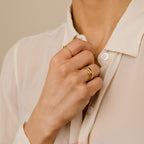 Close-up of a hand wearing the Duo Form Ring Set paired with other minimalist gold rings, styled with a cream button-up blouse.