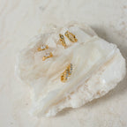 Five Aurora Huggies, featuring various designs and intricate diamond details, displayed on a large, textured white crystal stone.