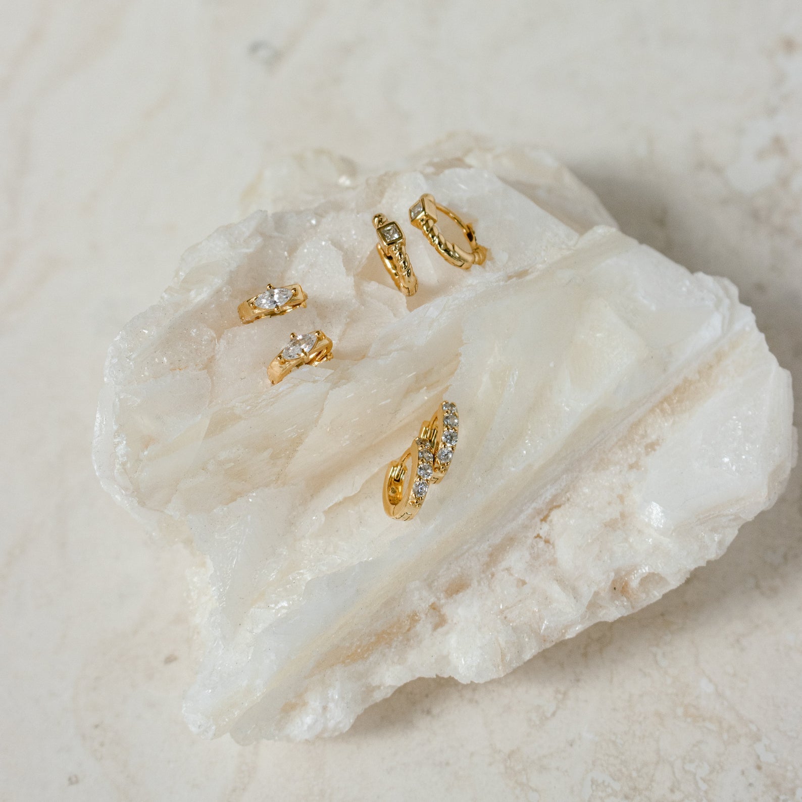 Five Aurora Huggies, featuring various designs and intricate diamond details, displayed on a large, textured white crystal stone.