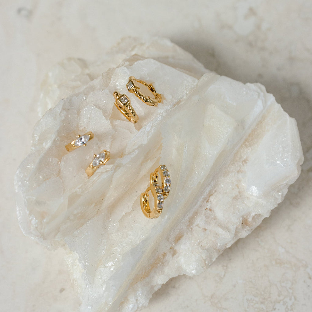 Four gold Willow Huggies, adorned with crystals and crafted from 925 Sterling Silver, are displayed on a large white crystal stone against a light background.