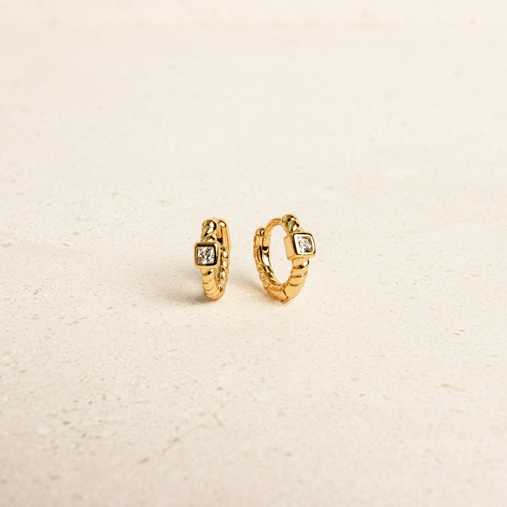 The Willow Huggies are small gold hoop earrings with a square gemstone, crafted from 925 Sterling Silver and displayed on a light beige surface.