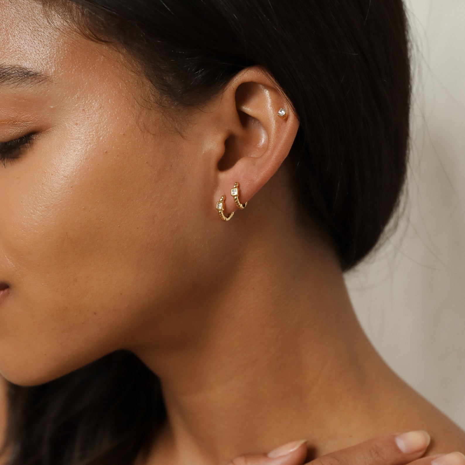 Close-up of a woman’s ear wearing two gold Willow Huggies and a small stud on the upper ear, highlighting her smooth skin.