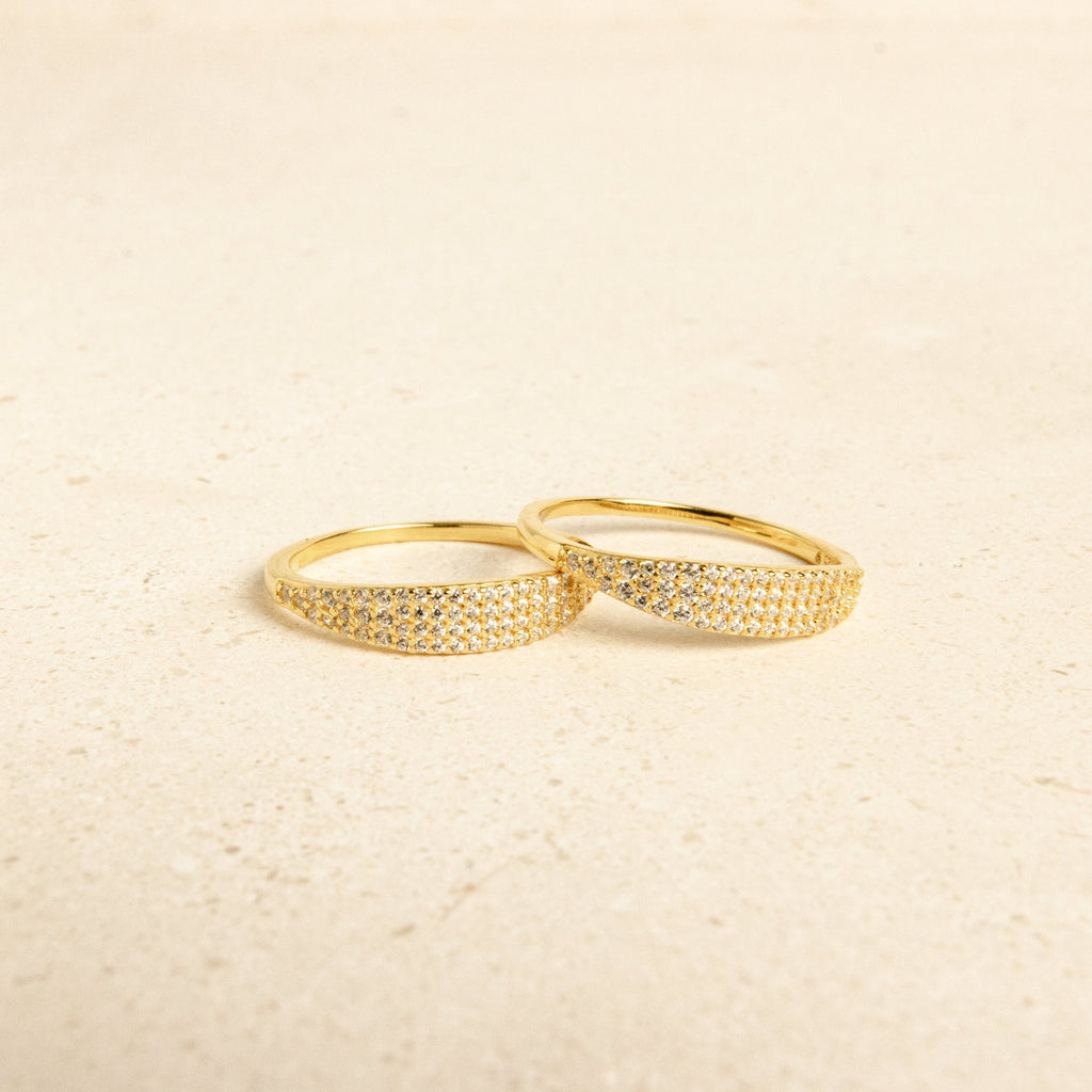 Two Gina Pave Signet Rings, featuring gold bands accented with small sparkling stones, are placed side by side on a light, textured surface.