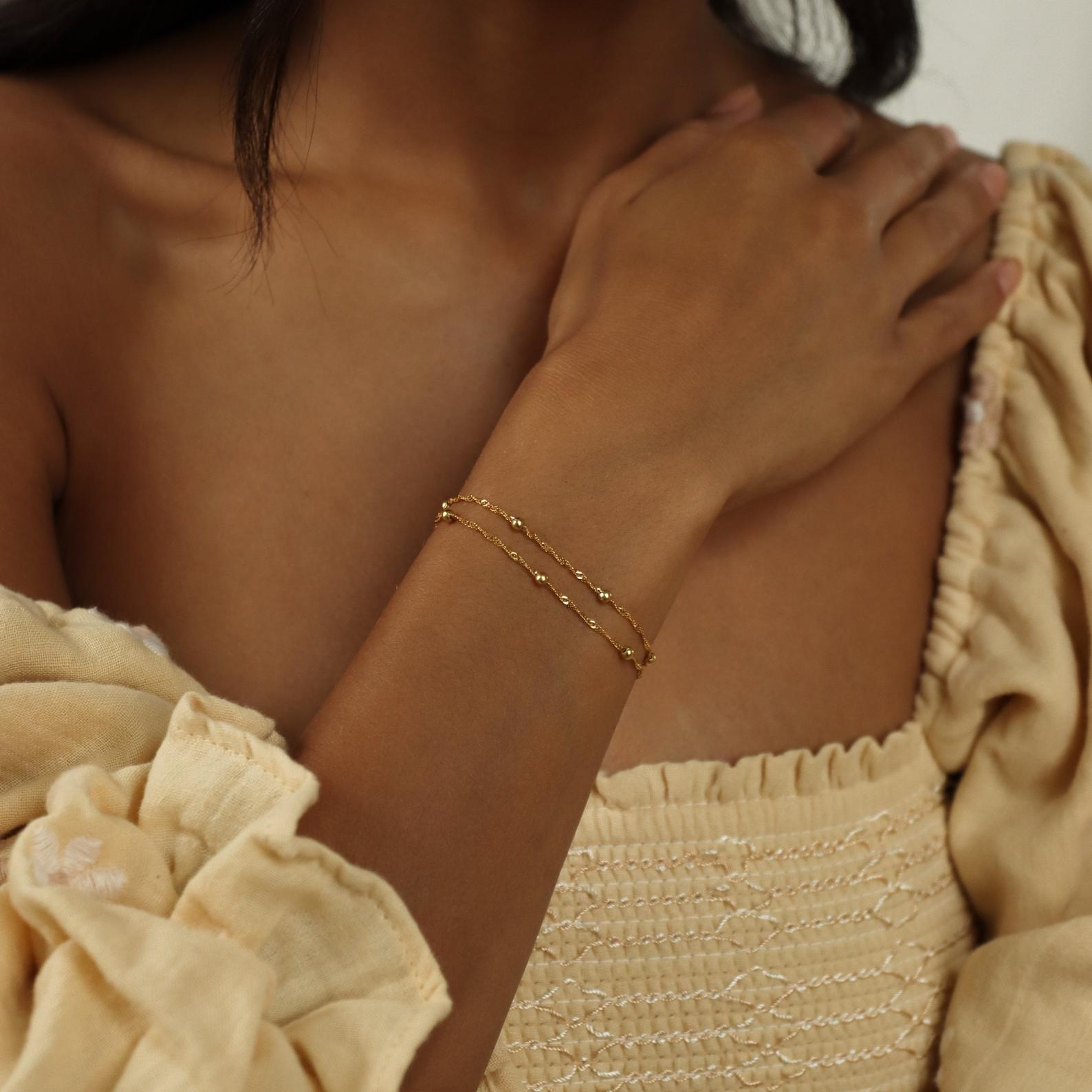 A woman in a beige dress wears the Duo Bead Chain Bracelet in Sterling Silver on her wrist, hand resting gently on her shoulder.