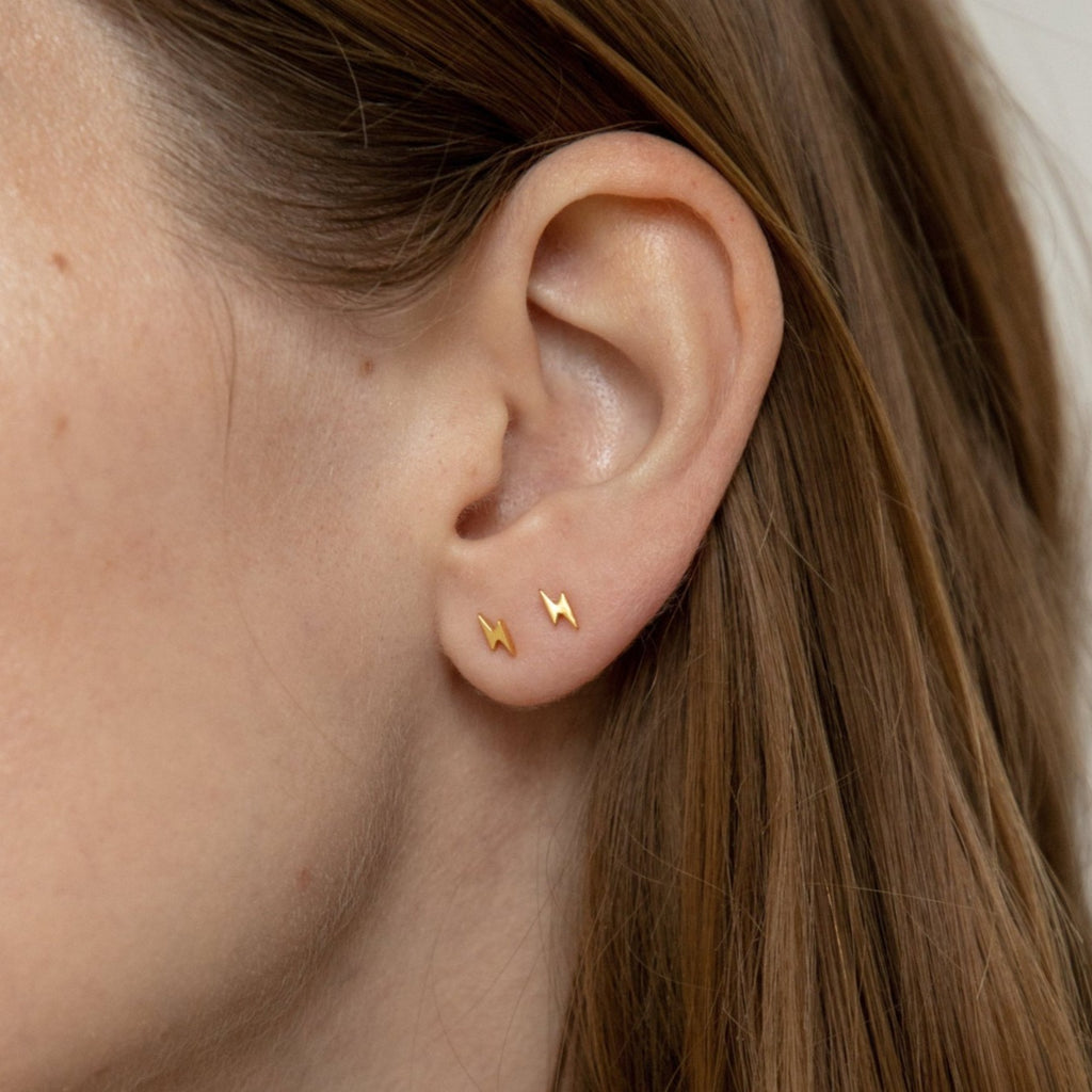 A close-up of an ear wearing two Lightning Bolt Studs, showcasing this edgy jewelry style on the earlobe.